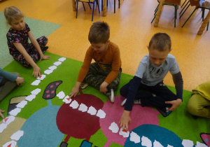 Trójka dzieci przelicza szablony mapy Polski ułożone w szeregu, odwracają piąty z kolej.